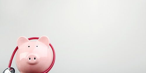 Pink piggy bank with stethoscope on wooden table