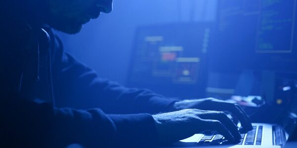 Close-up of professional computer hacker writing data codes typing on laptop at night in the office.