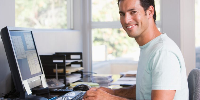 Man in home office using computer and smiling